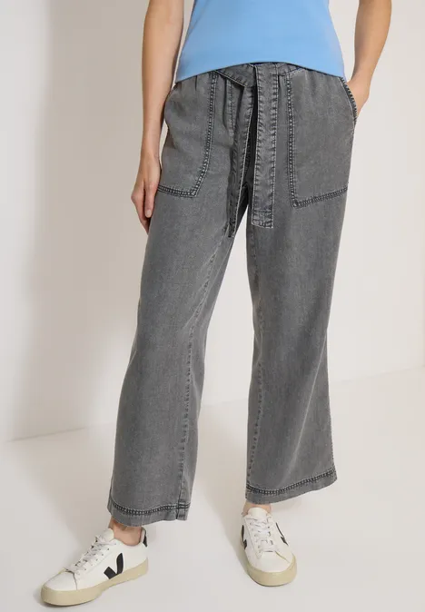 Weit geschnittene graue Jeans mit aufgesetzten Taschen, hoher Taille und weißen Sneakern.