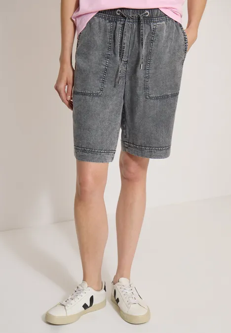 Shorts met Wide Leg pijpen en een Loose Fit pasvorm mid grey random wash Persoon in grijze spijkershorts met zakken en witte sneakers tegen een neutrale achtergrond.