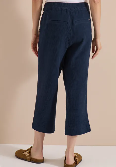 Vue arrière: pantalon large bleu foncé, longueur cheville, poches plaquées, mocassins marron, fond beige.