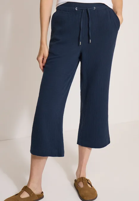 Un pantalon bleu marine mi-long ample avec cordon et poches, porté avec des chaussures marron.