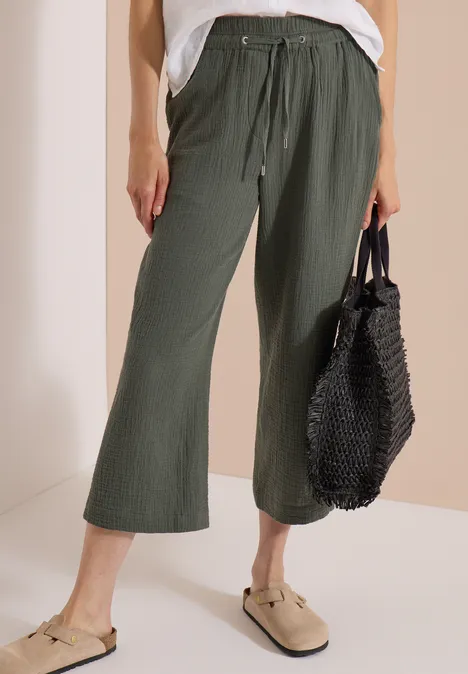 3/4 Wide Leg Hose in Musselin-Qualität clear khaki Frau trägt olivgrüne weite Culotte-Hose mit Tunnelzug, beigen Mules und schwarze Netz-Tasche