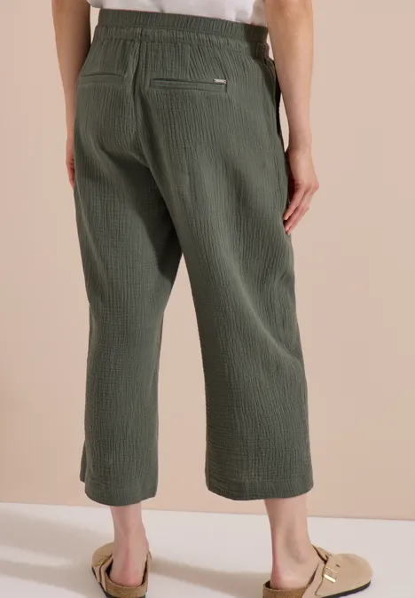 3/4 Wide Leg Hose in Musselin-Qualität clear khaki Rückansicht einer Person in weiten, knöchellangen, olivgrünen Hosen vor neutralem Hintergrund.