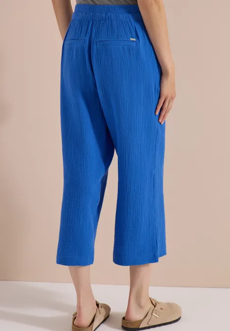 3/4 Wide Leg Hose in Musselin-Qualität surf blue Blaue, plissierte 7/8-Hose mit elastischem Bund, weit geschnitten, kombiniert mit beigen Sandalen.