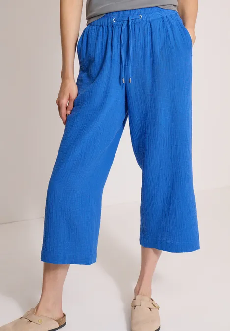3/4 Wide Leg Hose in Musselin-Qualität surf blue Frau trägt blaue, weit geschnittene Culotte-Hose mit Kordelzug und strukturierter Oberfläche, kombiniert mit beigen Flats.