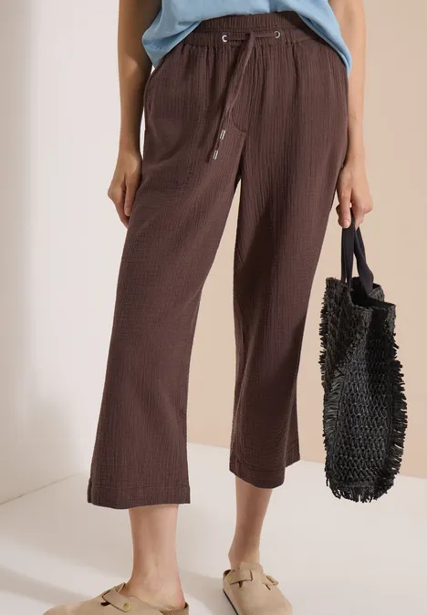 Frau mit brauner 3/4-Hose, hellblauem Top, beigen Sandalen und schwarzer Korbtasche.