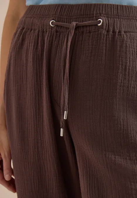 Nahaufnahme einer braunen, texturierten Hose mit elastischem Bund und Kordelzug mit silbernen Endkappen.