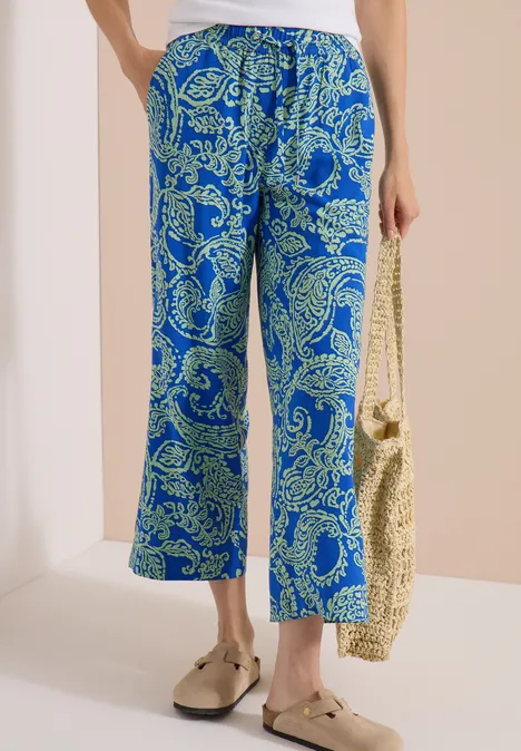 7/8 High Waist Wide Leg Hose im Loose Fit surf blue Blaue Hose mit weitem Bein und grünen Paisley-Muster, kombiniert mit Basttasche und goldenen Schuhen.