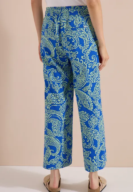 7/8 High Waist Wide Leg Hose im Loose Fit surf blue Rückansicht einer Person in weiten Hosen mit blau-grünem Paisley-Muster und flachen Sandalen.