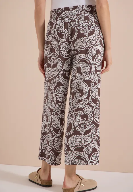 7/8 High Waist Wide Leg Hose im Loose Fit brown cacao Rückenansicht einer Person in braunen, knöchellangen Culottes mit weißem Paisley-Muster und beige Loafers.