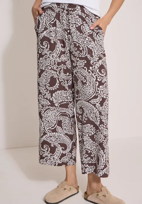7/8 High Waist Wide Leg Hose im Loose Fit brown cacao Braune, weite Hose mit weißen Paisley-Prints und Taschen, kombiniert mit beigen Pantoletten.