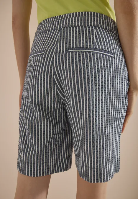 Rückansicht einer Person in blau-weiß gestreiften Shorts und grünem Oberteil