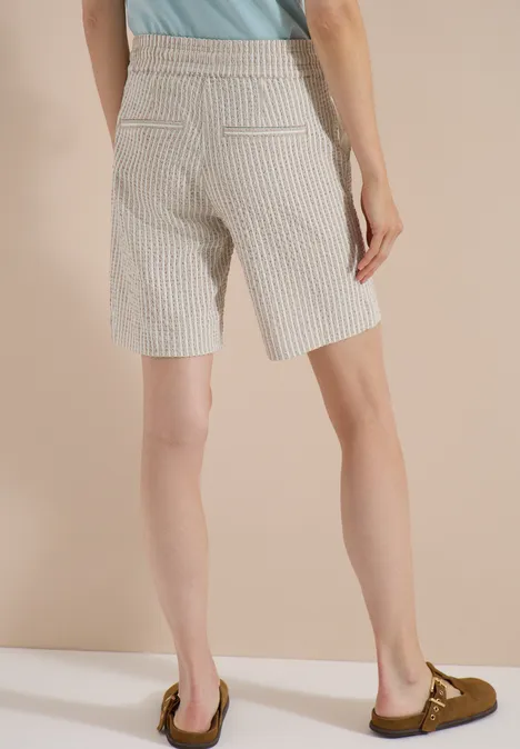 Person in hoch taillierten, gestreiften Bermudashorts, von hinten fotografiert, mit Mokassins.