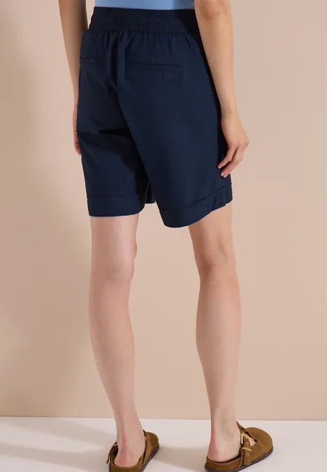 High Waist Wide Leg Shorts im Loose Fit universal blue Rückansicht einer Person in marineblauen Bermudashorts und braunen Mokassins vor hellem Hintergrund.