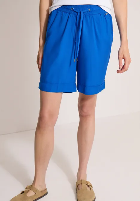 High Waist Wide Leg Shorts im Loose Fit surf blue Eine Person trägt knielange, leuchtend blaue Shorts mit Kordelzug und beige Sandalen.
