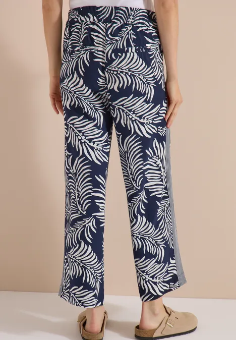 Vue de dos d’un pantalon ample bleu marine à motif de feuilles tropicales blanches.