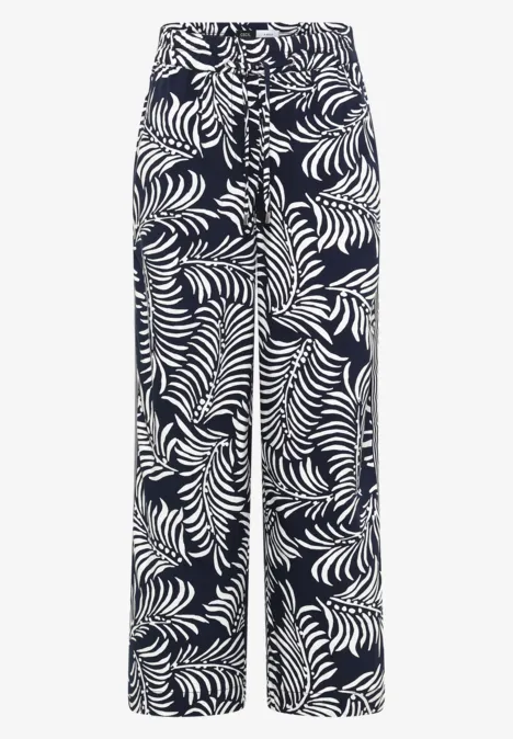 Pantalon ample à fond sombre et motif feuille tropicale blanc.