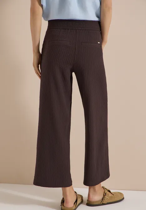 Achteraanzicht van een persoon met bruin geribd, wijd broek en kaki espadrilles.