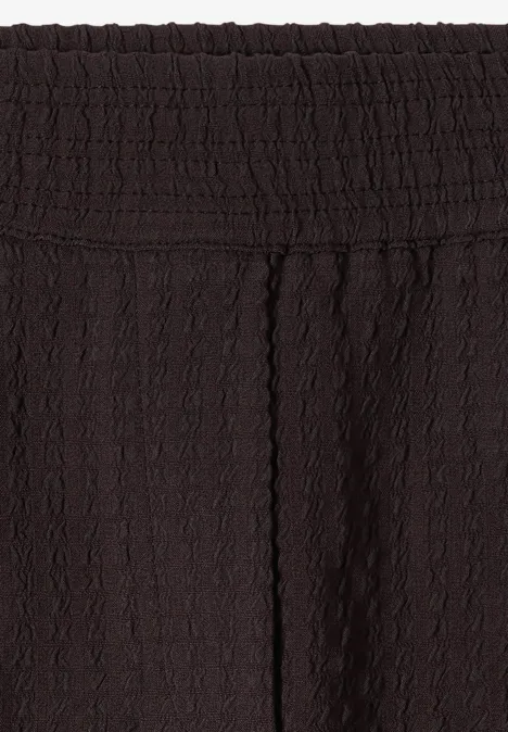 Close-up van een zwart kledingstuk met elastische tailleband en fijne, gestructureerde stof.