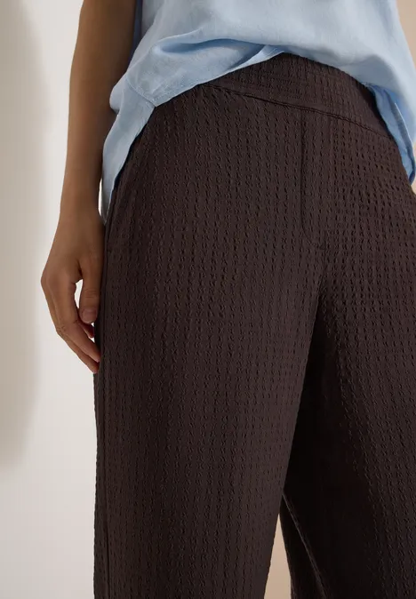 Close-up van een bruin textuurbroek met hoge taille en een lichtblauw shirt.