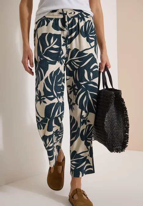 Broek met High Waist en Wide Leg pijpen in een Loose Fit pasvorm palm breeze green Luchtige, lichte broek met donkergroene bladprint, bruine loafers en zwarte gevlochten tas.