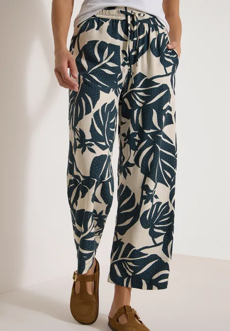 Broek met High Waist en Wide Leg pijpen in een Loose Fit pasvorm palm breeze green Losvallende broek met donker bladpatroon op lichte achtergrond, gecombineerd met bruine mocassins.