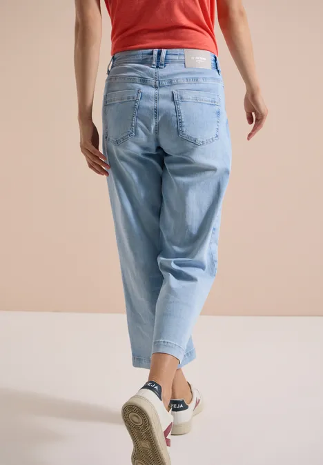 Jean 7/8 Wide Leg avec détail crocheté light blue random bleached Person in rotem Top und hellblauen Jeans von hinten, mit weißen Sneakern.