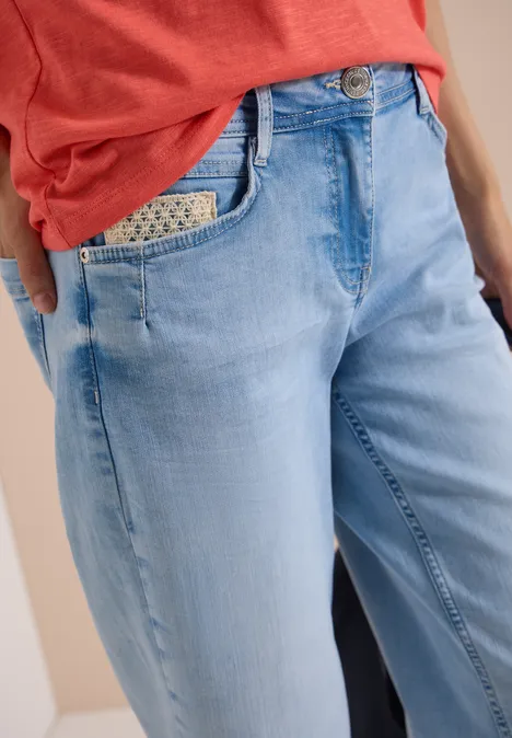 Jean 7/8 Wide Leg avec détail crocheté light blue random bleached Frau trägt helle, locker sitzende Jeans mit gemustertem Einstecktuch in der Tasche und rotem Shirt.