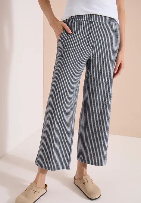 Weite, knöchellange Hose in Navy mit feinen weißen Streifen, seitlichen Taschen, kombiniert mit beigen Pantoletten.