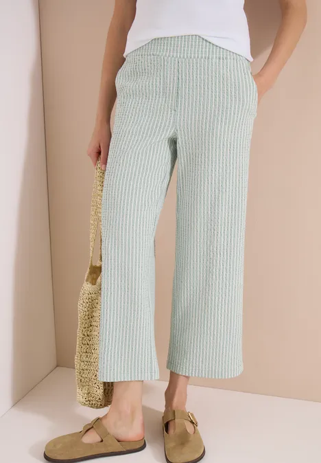 Damen-Culotte mit grün-weißen Streifen, kombiniert mit weißem Top, Basttasche und Pantoletten.