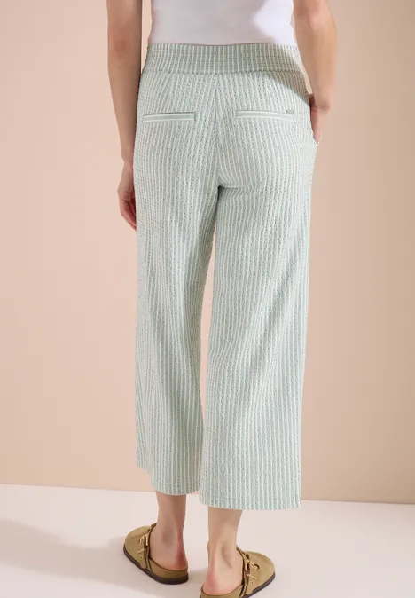 Rückenansicht: Weite, knöchellange Stoffhose mit grünen und weißen Streifen, zwei Paspeltaschen und Sandalen.