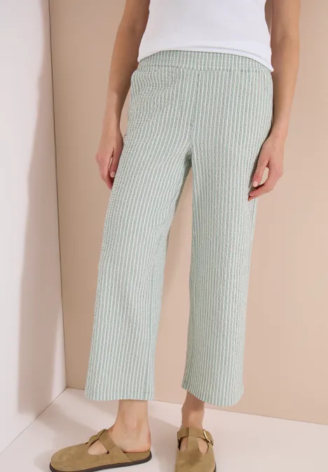 Frau in weißem Top, grün-weiß gestreifter, weiter Culotte und beigen Tassel-Mokassins.