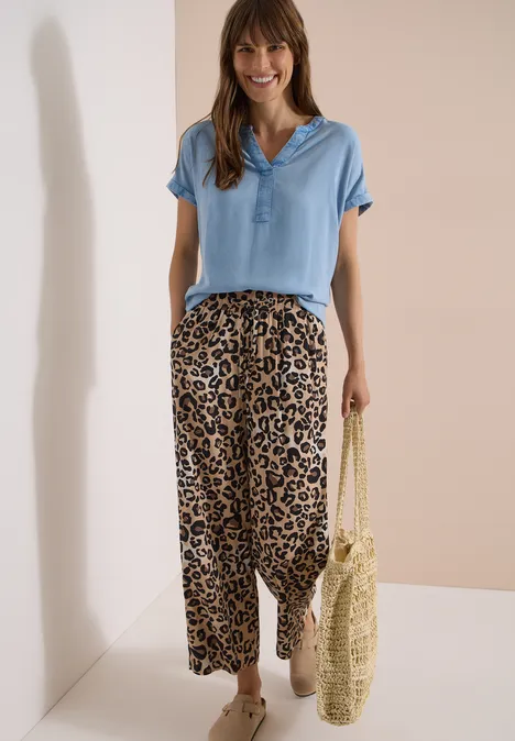 High Waist Wide Leg Hose mit Leo-Print urban taupe Frau trägt hellblaues Poloshirt, weite Leopardenhose und Strohtasche vor neutralem Hintergrund.