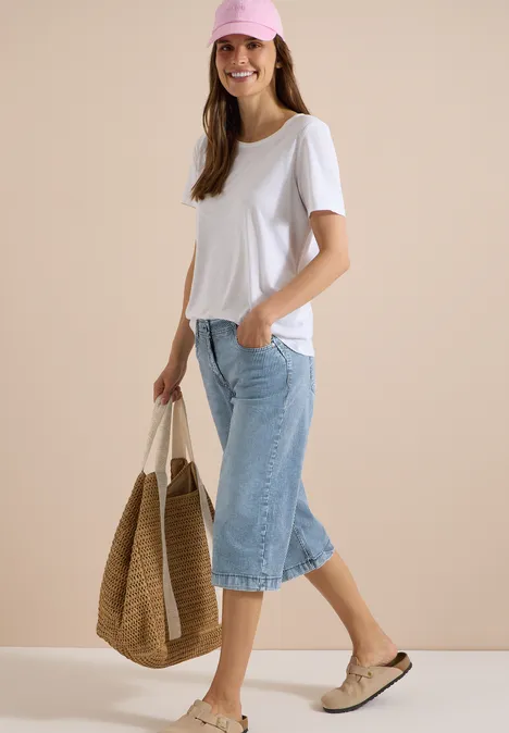 Femme en t-shirt blanc et pantacourt en jean, sac en paille et mocassins.