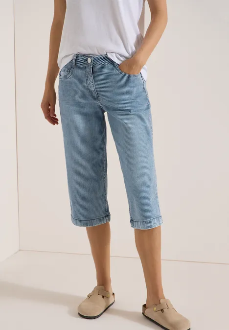 Personne porte un t-shirt blanc, un jean capri bleu clair et des mocassins beiges devant un fond clair.