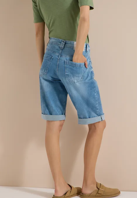 Vue arrière d'une personne en T-shirt vert et bermuda en jean bleu retroussé, portant des sandales marrons.