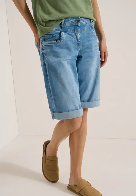 Demi-corps d'une personne portant un short en jean bleu clair jusqu'aux genoux et des mocassins marron.