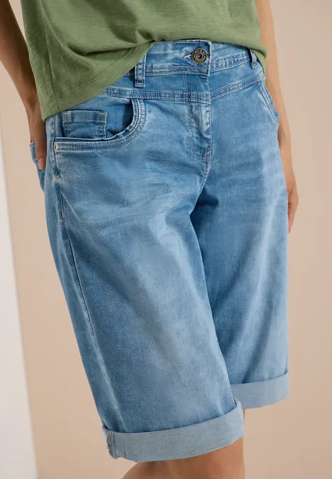 Une personne porte un t-shirt vert et un bermuda en jean bleu clair aux revers.