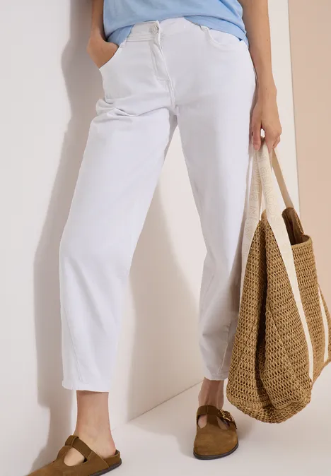 Jean taille haute à Barrel Leg, coupe ample White Personne porte un jean blanc ample, des sabots marron et tient un sac en paille