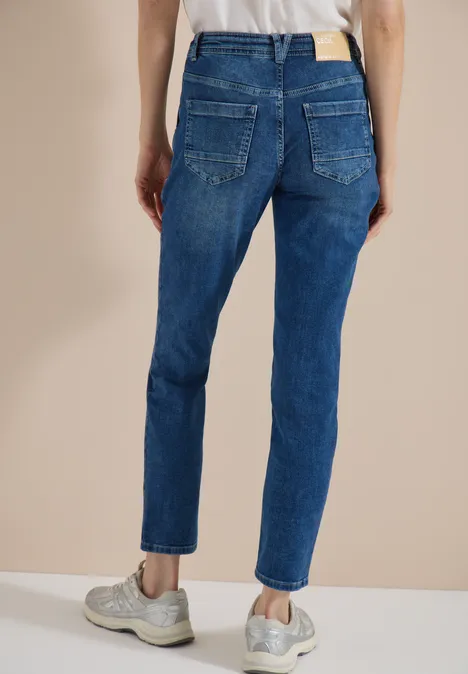 Straight Leg Jeans mit Gürteldetail mid blue used wash Rückansicht einer Person in blauen Jeans und grauen Sneakern vor neutralem Hintergrund.