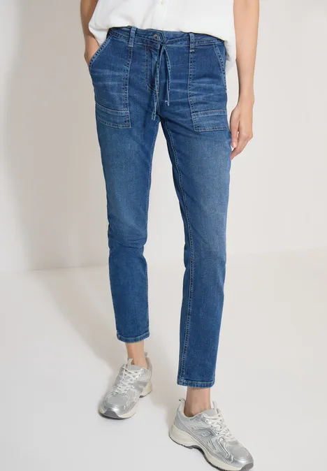 Straight Leg Jeans mit Gürteldetail mid blue used wash Blaue Denim-Jogginghose mit Kordelzug und aufgesetzten Taschen, kombiniert mit silbernen Sneakern.