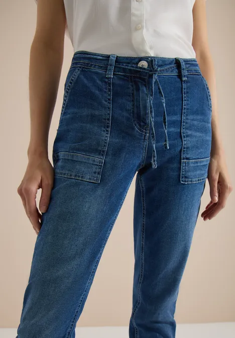 Straight Leg Jeans mit Gürteldetail mid blue used wash Frau trägt hellblaues Hemd und lässige Jeans mit aufgesetzten Taschen.