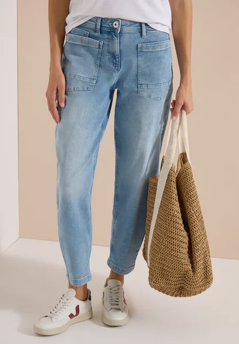 Barrel Leg Jeans mit aufgesetzten Taschen light blue used wash Person trägt helle Jeans, weiße Sneaker und hält eine geflochtene Strohtasche.