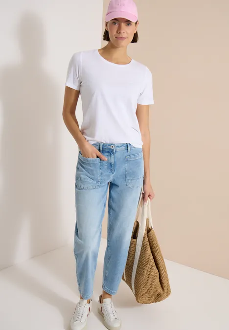 Barrel Leg Jeans mit aufgesetzten Taschen light blue used wash Frau in weißem T-Shirt, hellblauen Jeans und weißen Sneakern hält eine große Strohtasche.