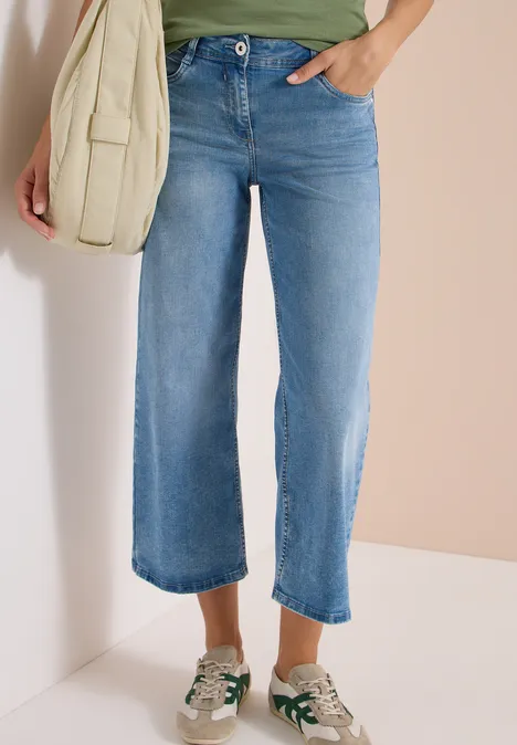Lichtblauwe cropped jeans met rechte pijpen, gecombineerd met witte sneakers en een beige schoudertas.
