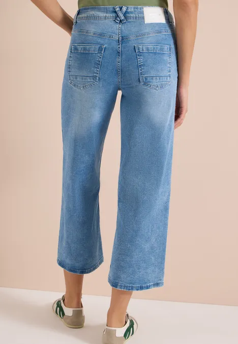 Achteraanzicht van een persoon in lichtblauwe, wijdvallende jeans en witte sneakers