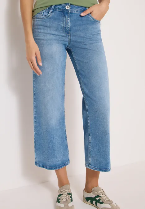 Lichtgekleurde, wijde cropped jeans op enkelhoogte, gecombineerd met witte sneakers met groene details.