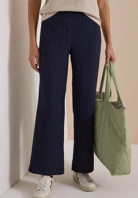 Wide Leg Hose mit Strukturstreifen urban dark blue Frau in locker sitzender navy Nadelstreifenhose, weißem Shirt, weißen Sneakern und grüner, gesteppter Tasche.