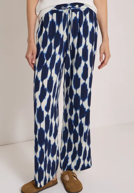 Pantalon large à motif abstrait bleu et blanc, taille élastiquée avec lien, poches latérales, porté avec mocassins marron.