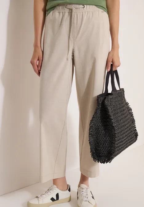 Bas du corps, pantalon beige en lin, baskets blanches et grand sac noir en maille.