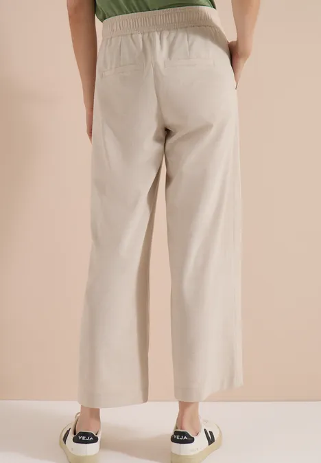 Vue arrière d'une personne portant un pantalon large beige à taille élastique et des espadrilles noires.